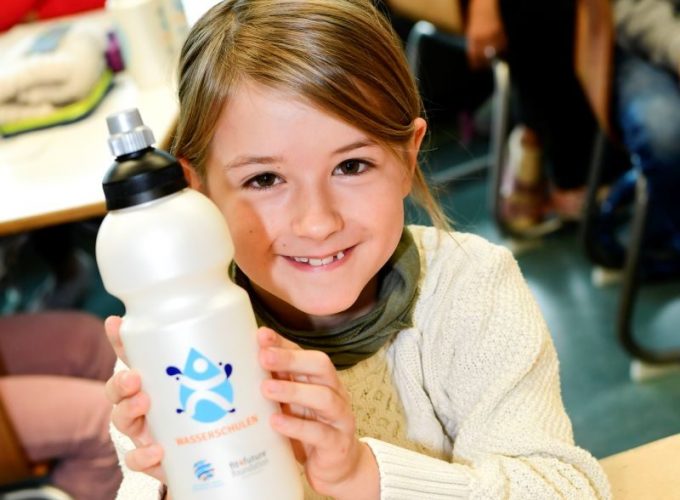 Mädchen lächelt und hält Wasserflasche in den Händen.