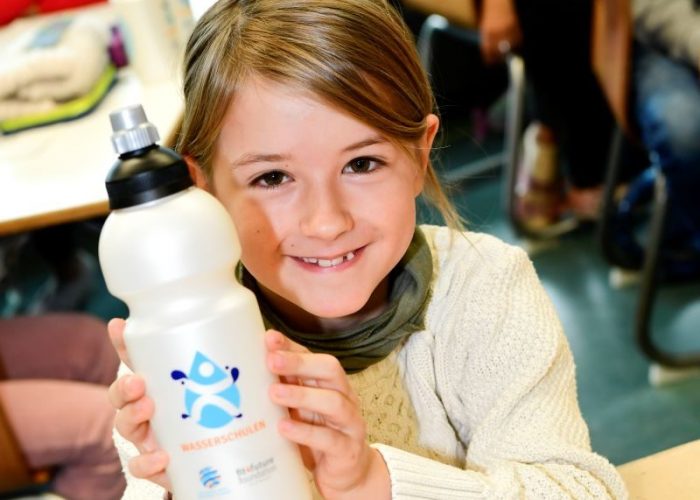 Mädchen lächelt und hält Wasserflasche in den Händen.